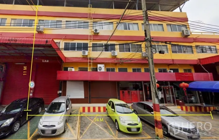 Warehouse for rent in Bang Phli, Samut Prakan - Front view of a red and yellow commercial building with marked parking bays and annotated frontage near roller shutter doors.