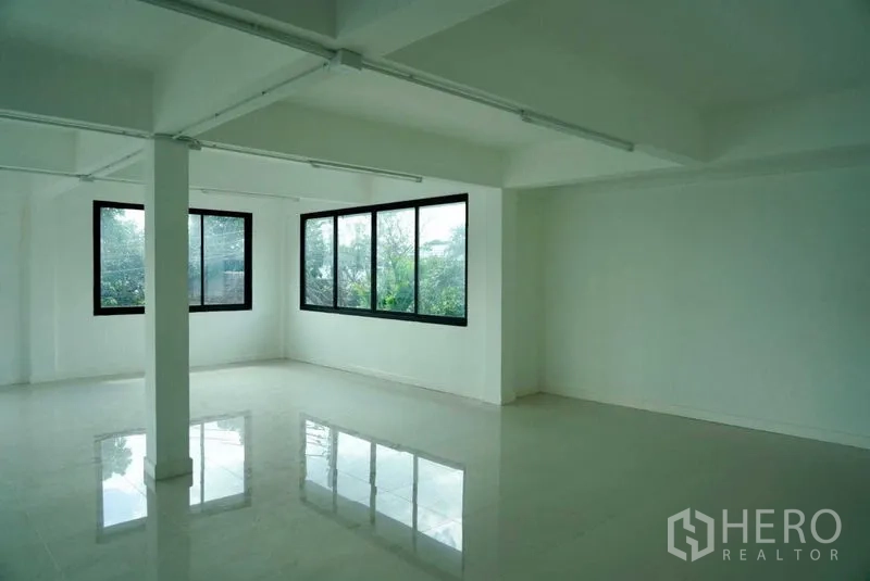 Office Space for sale in Khan Na Yao, Bangkok - Corner office area with large black-framed windows and reflective flooring overlooking greenery.