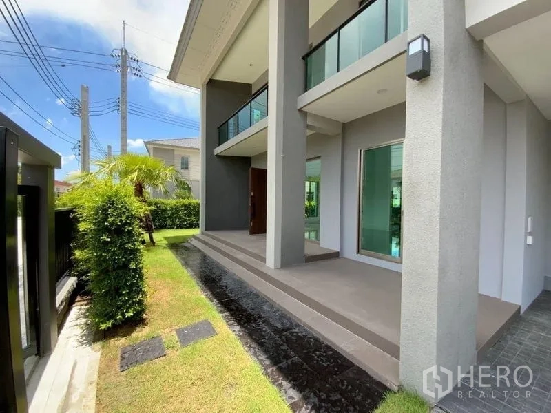 联排别墅 出租在Prawet, Bangkok - 房屋前廊，高立柱与小草坪，上层设阳台。