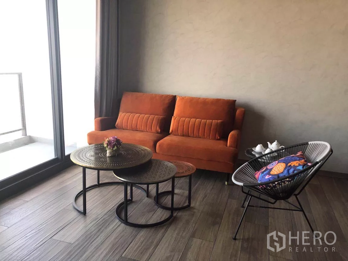 คอนโด ขายในWatthana, Bangkok - มุมนั่งเล่นอบอุ่นด้วยโซฟาสีส้ม โต๊ะกลางทรงกลมซ้อนกัน และประตูกระจกบานใหญ่เชื่อมต่อระเบียง