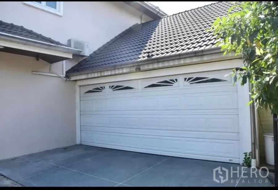 独立式住宅 出售在Sai Mai, Bangkok - 双车位车库，白色分段式车库门与瓦顶屋檐。