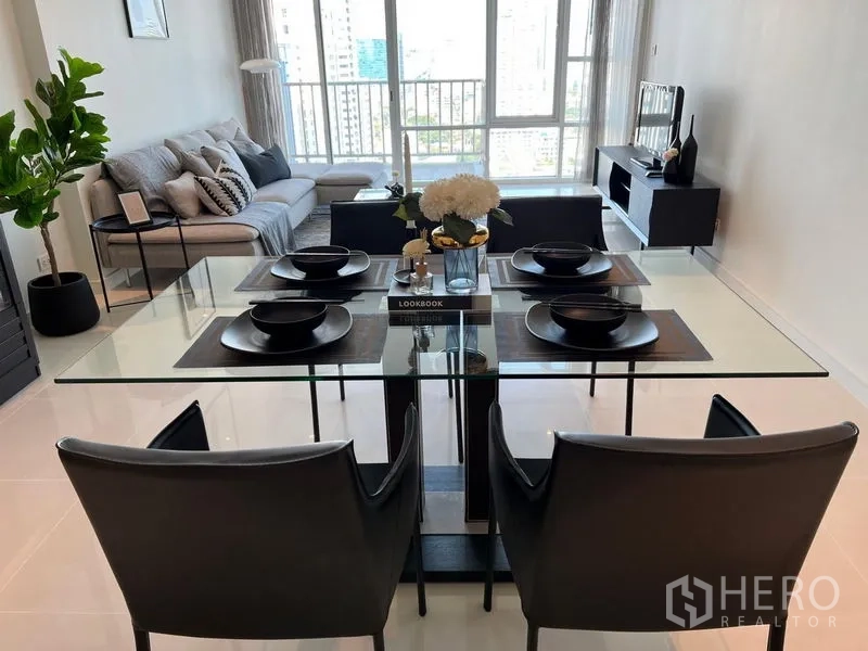 公寓 出租在Watthana, Bangkok - 开放式客餐厅，玻璃餐桌、沙发，落地窗带曼谷城市景观。