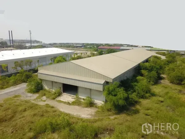 工厂 出售在Samut Prakan - 俯瞰金属屋顶的长条形工厂仓库，周围绿化与工业区景观