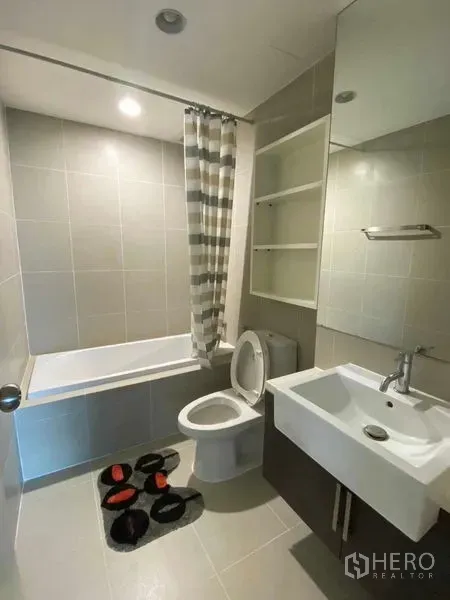 Condominium for rent in Khlong Toei, Bangkok - Modern bathroom with bathtub, striped shower curtain, square basin and open wall shelving.