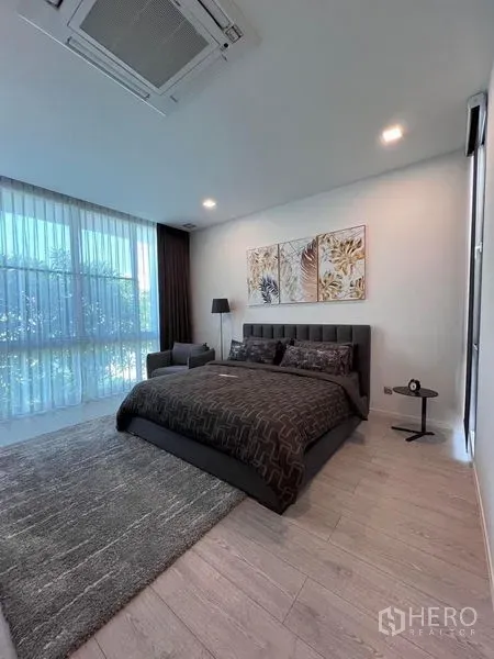 Detached House for sale in Samut Prakan - Bright bedroom with large windows, sheer curtains, and a dark upholstered bed.