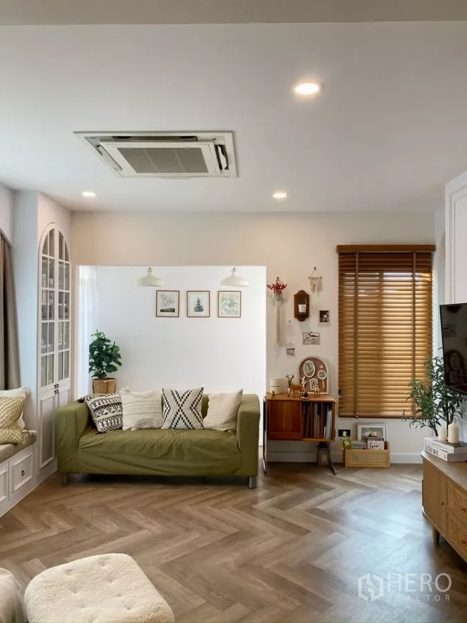 独立式住宅 出售在Sai Mai, Bangkok - 客厅配绿色沙发、木质百叶与人字拼木地板。