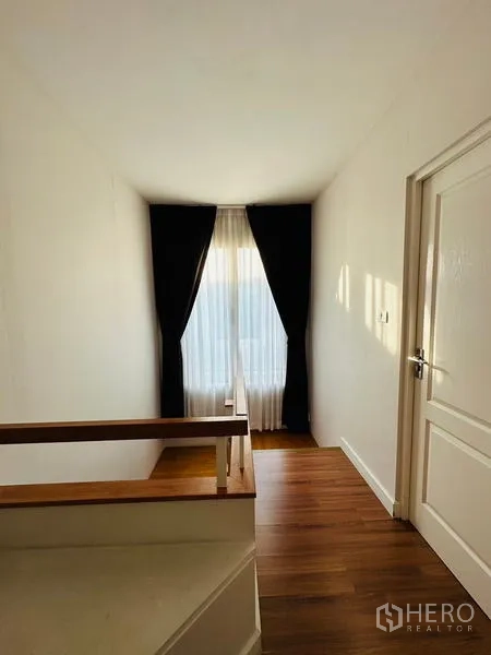 Detached House for sale in Prawet, Bangkok - Stair landing filled with natural light, wood floors and curtain-dressed window.