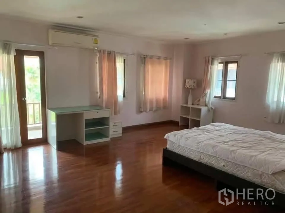Townhouse for rent in Watthana, Bangkok - Spacious bedroom with balcony door, desk, and bed, featuring wood flooring.