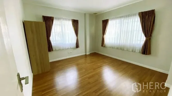 Detached House for rent in Bang Kapi, Bangkok - Empty bedroom with two large windows, sheer curtains and wood floors.