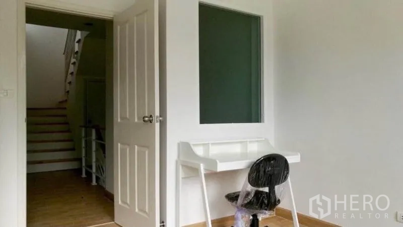 Townhouse for rent in Wang Thonglang, Bangkok - Compact study room with white desk and chair, interior window panel, and doorway to the staircase.