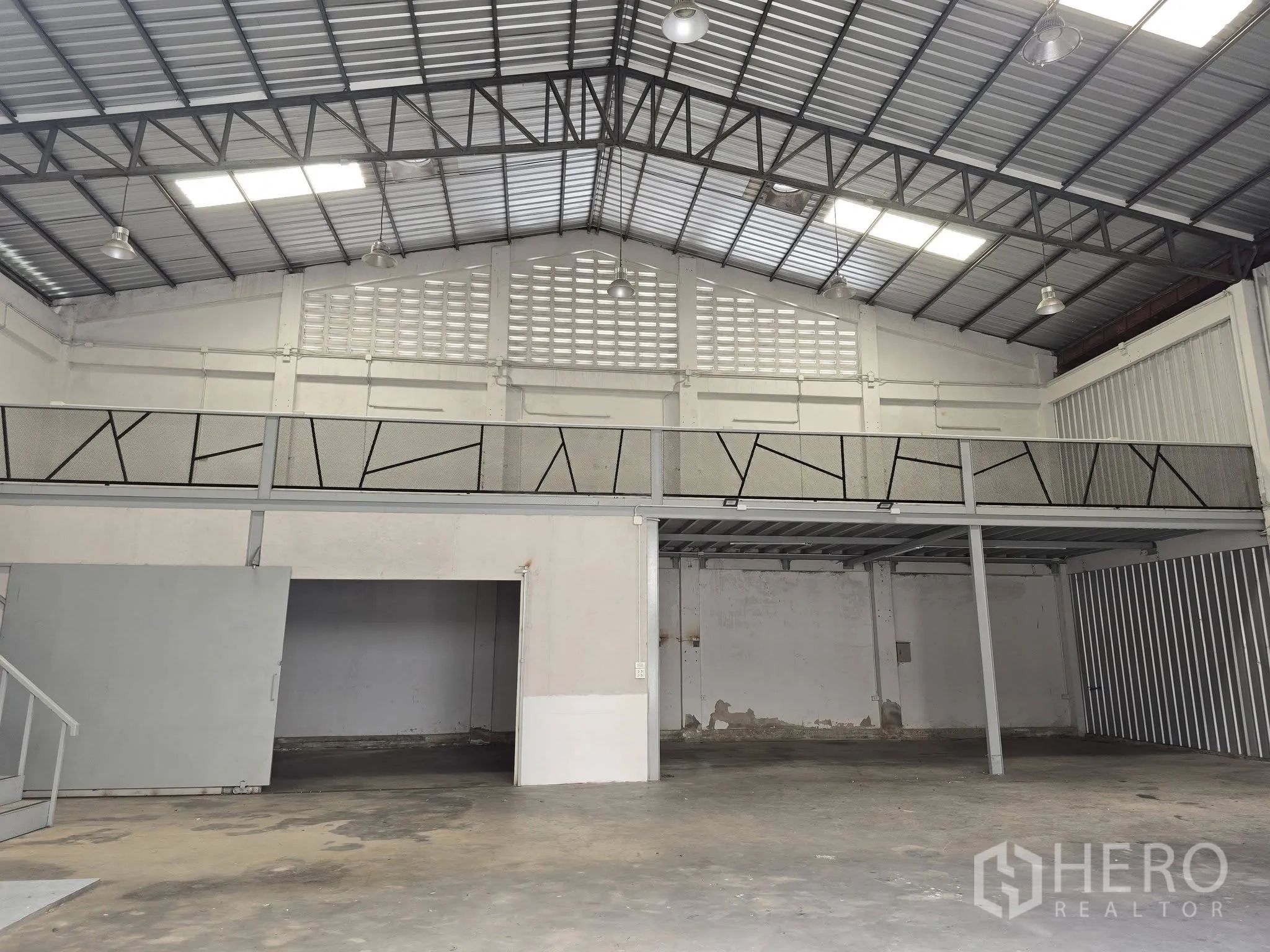 Warehouse for rent in Bang Na, Bangkok - Wide view of warehouse hall showing steel roof trusses, skylights, mezzanine walkway, and open floor area.
