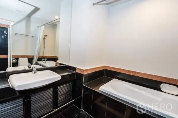 Apartment for rent in Sathon, Bangkok - Bathroom featuring a bathtub, vanity sink, large mirror, and black tile accents.