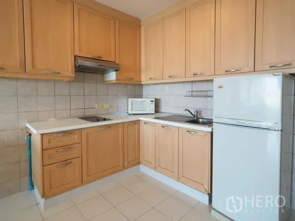 公寓 出租在Sathon, Bangkok - L形厨房配浅木柜体、炉灶、抽油烟机、微波炉与冰箱，曼谷公寓。