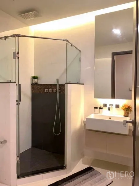 Condominium for rent or sale in Huai Khwang, Bangkok - Bright bathroom with glass shower enclosure, vanity, and rain shower.