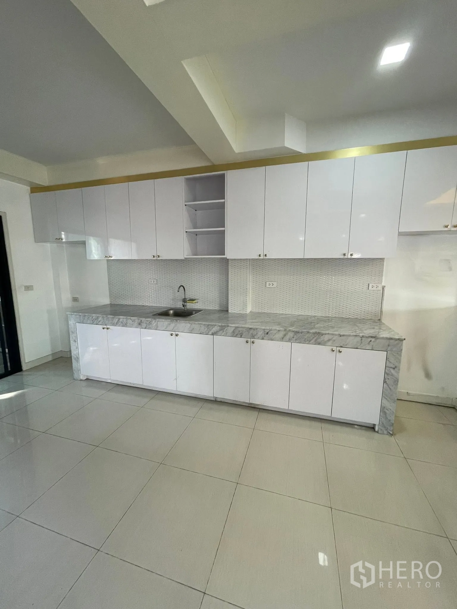 Detached House for rent or sale in Lam Luk Ka, Pathum Thani - Modern kitchen with white cabinets, marble-effect countertop, and recessed ceiling lights.