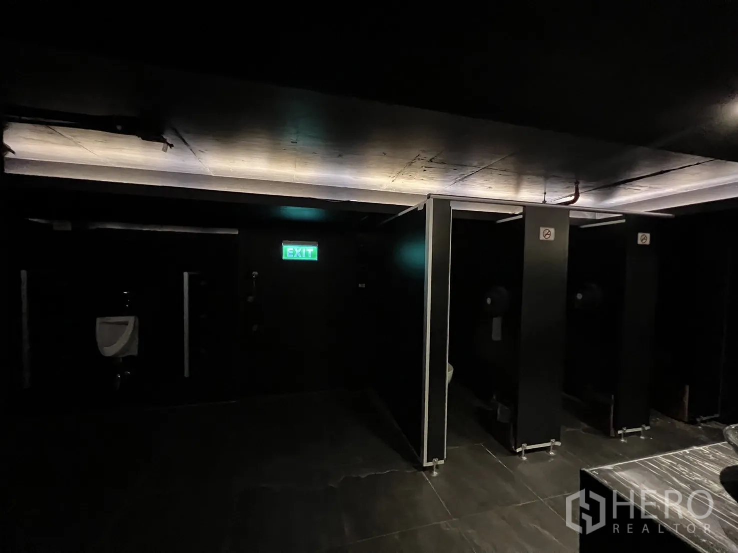 零售空间 出租 - 洗手间走道，隔间、小便池与发光出口标识。