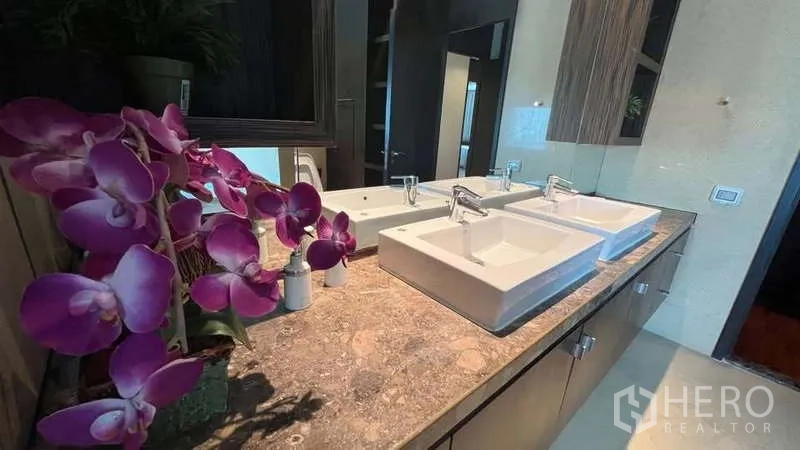 อพาร์ทเมนท์ ให้เช่าในPathum Wan, Bangkok - ห้องน้ำพร้อมอ่างล้างหน้าทรงสี่เหลี่ยมคู่ เคาน์เตอร์หินอ่อน กระจกบานใหญ่ และดอกกล้วยไม้ประดับ