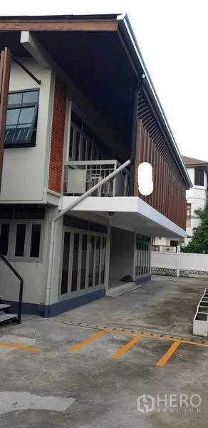 带办公室的家 出租在Chatuchak, Bangkok - 现代两层立面，木格栅外立面与划线停车区。