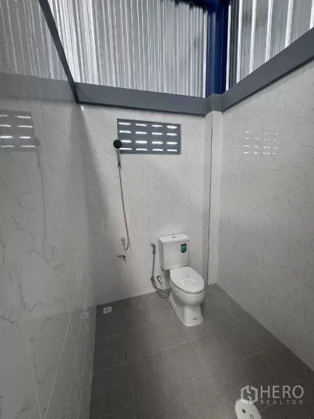 Warehouse for rent in Bang Phli, Samut Prakan - Clean tiled restroom inside the warehouse with toilet, handheld bidet and ventilated window.