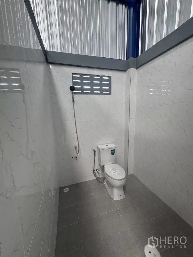 Warehouse for rent in Bang Phli, Samut Prakan - Clean tiled restroom inside the warehouse with toilet, handheld bidet and ventilated window.