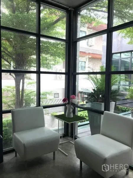 Office Space for rent in Bang Kapi, Bangkok - Lounge corner with two white chairs beside floor‑to‑ceiling windows overlooking greenery.