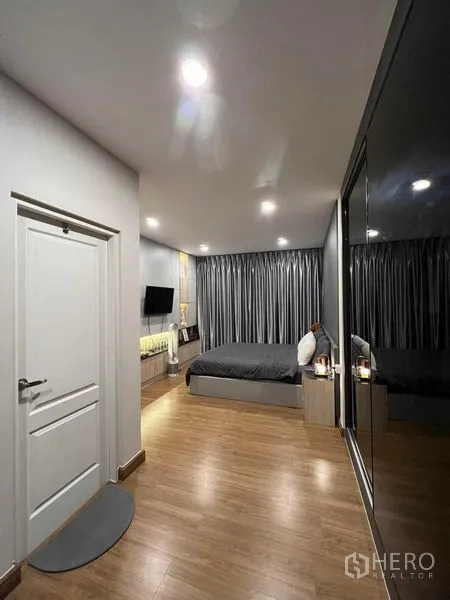 บ้าน ให้เช่าหรือขายในLat Krabang, Bangkok - มุมมองห้องนอนใหญ่ มีผ้าม่านสีเทา เตียง และตู้เสื้อผ้ากระจกเงา