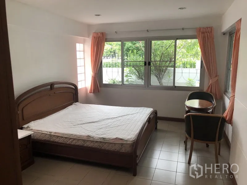 Detached House for rent in Khlong Toei, Bangkok - Ground-floor bedroom with corner windows overlooking the garden, bed and small table set.