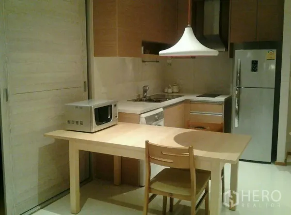 公寓 出租或出售在Khlong Toei, Bangkok - 紧凑的L形厨房，木质橱柜、餐桌、冰箱和微波炉。