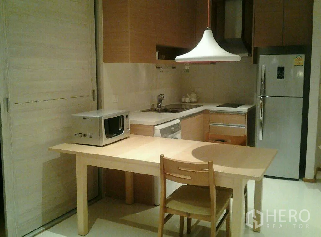 公寓 出租或出售在Khlong Toei, Bangkok - 紧凑的L形厨房，木质橱柜、餐桌、冰箱和微波炉。