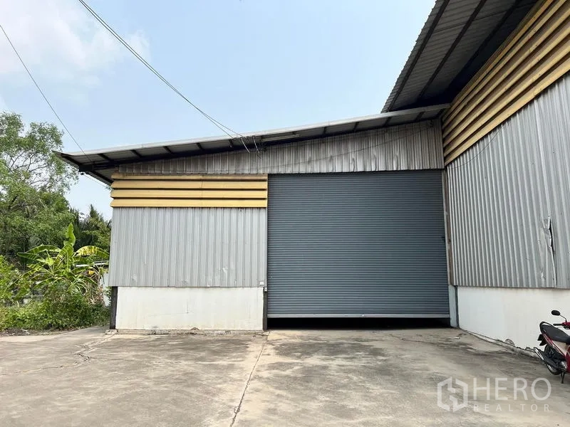 Warehouse for rent in Phra Samut Chedi, Samut Prakan - Metal-clad warehouse facade with a large roller shutter and paved apron.