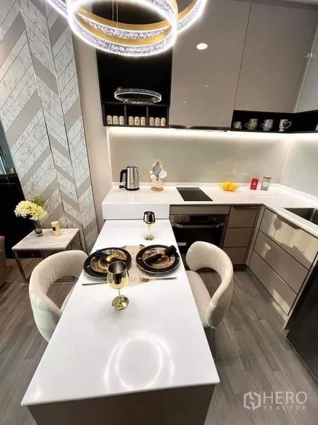 Condominium for sale in Bang Sue, Bangkok - Modern kitchenette with glossy cabinets, white L-shaped counter, two-seat dining bar and ring chandelier.