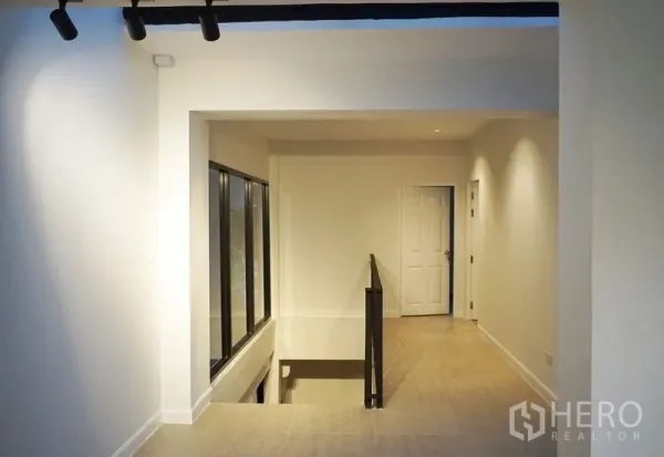 带办公室的家 出租或出售在Watthana, Bangkok - 明亮的二层走廊，侧面大窗、楼梯挑空与简洁白墙。