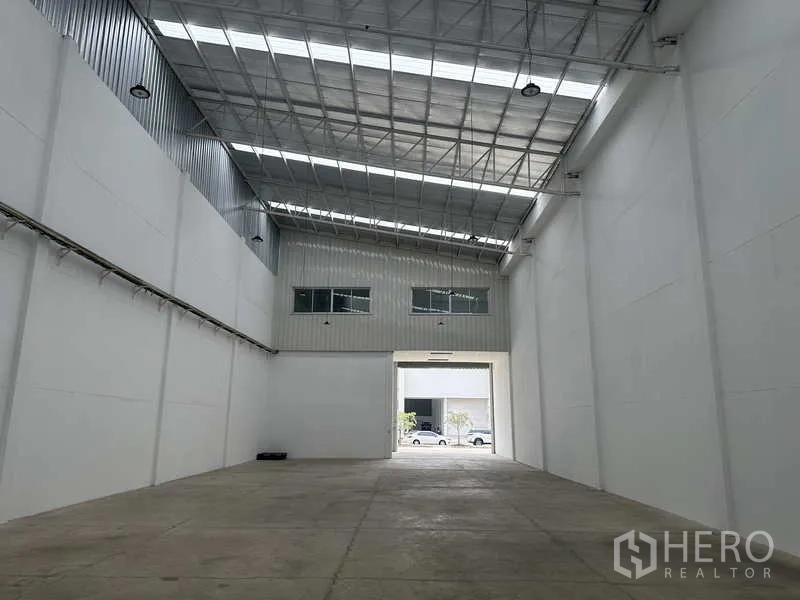 Factory for rent in Khlong Luang, Pathum Thani - High-bay warehouse interior with skylights and large roller door opening to the forecourt.