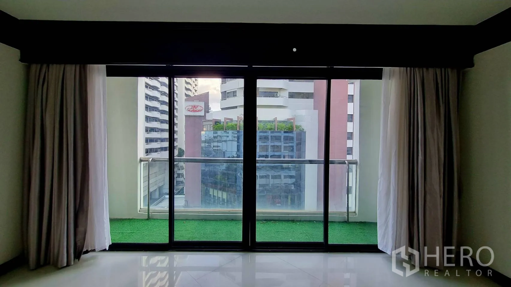 公寓 出租在Watthana, Bangkok - 绿色人造草坪阳台，透过玻璃门观赏城市景。