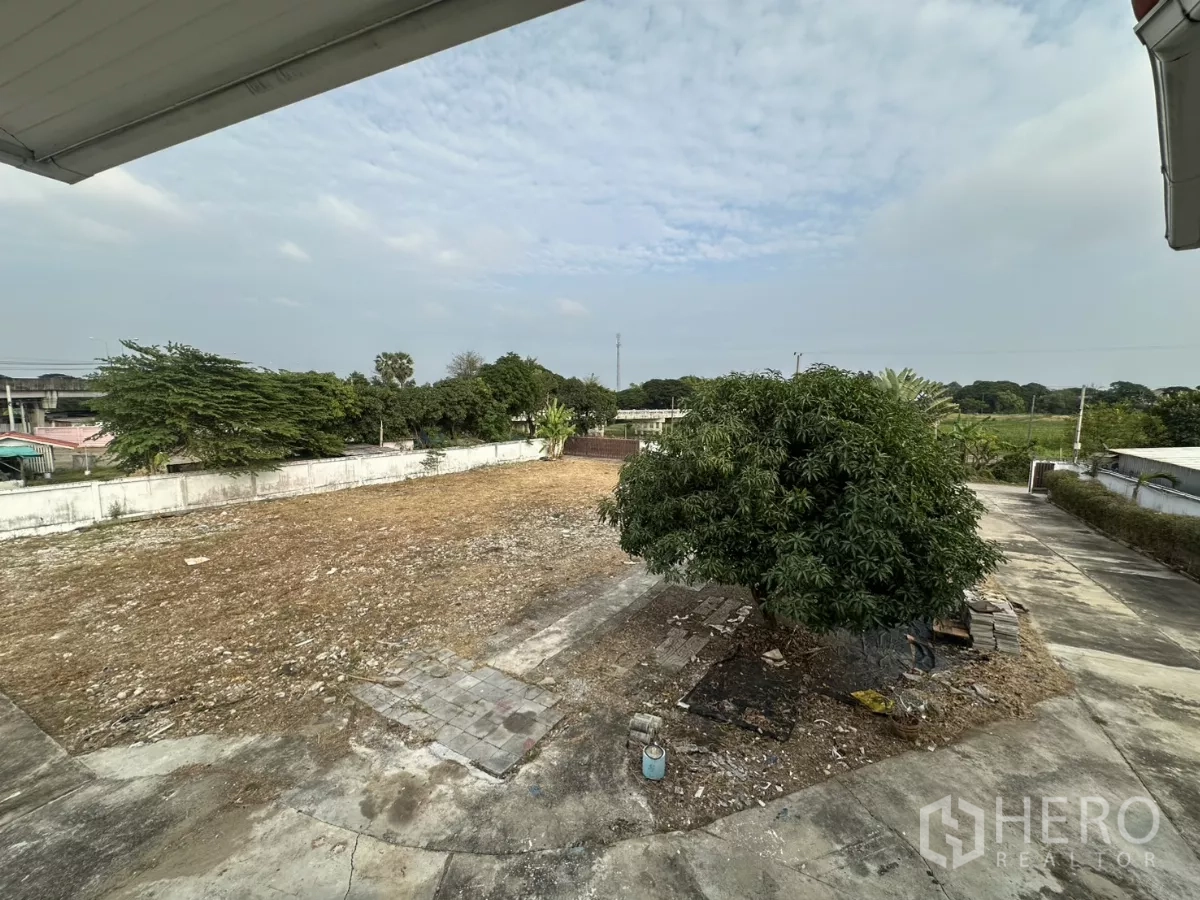 สำนักงานที่บ้าน ให้เช่า - ภาพมุมสูงของสนามว่างกว้างพร้อมต้นมะม่วงและกำแพงรอบ.