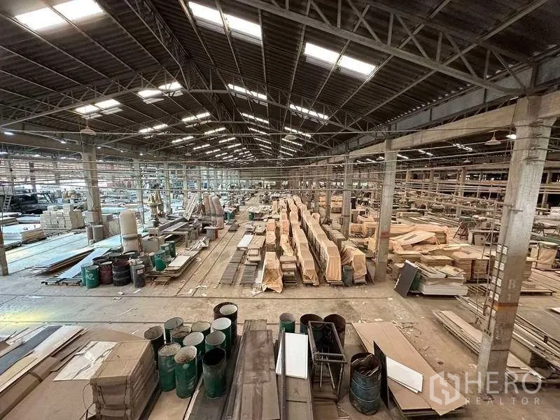 工厂 出租在Sai Noi, Nonthaburi - 大型仓储空间，木料堆与桶装物资，位于采光良好的金属屋架下。