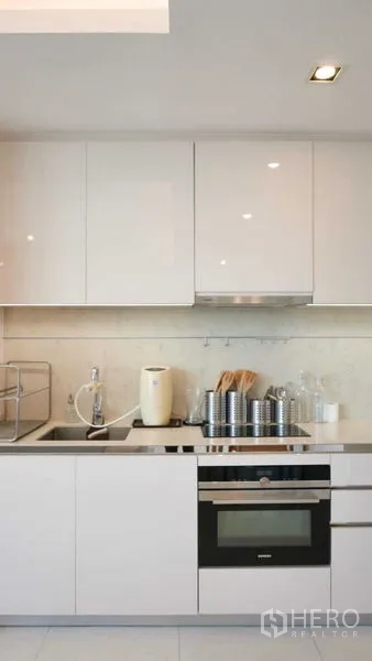 Condominium for rent in Sathon, Bangkok - Sleek white kitchen with built-in oven, sink and glossy cabinets.