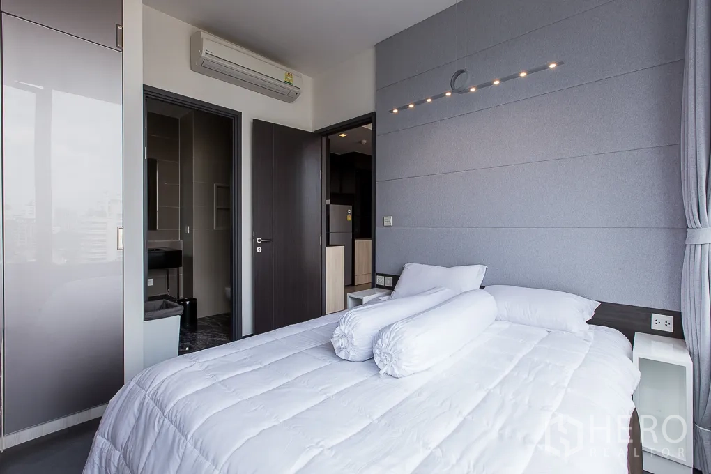 Condominium for rent in Watthana, Bangkok - Cozy bedroom with grey accent wall, modern lighting and ensuite access.