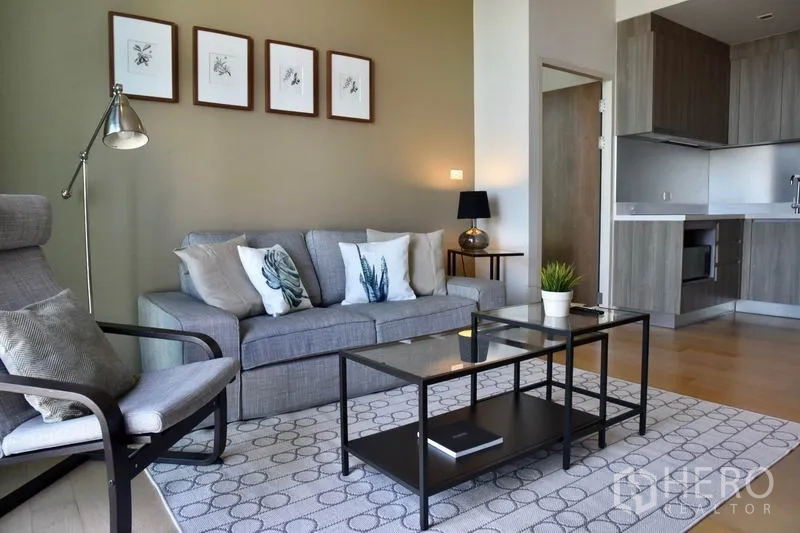 คอนโด ให้เช่าในPhaya Thai, Bangkok - ห้องนั่งเล่นสว่างพร้อมโซฟาสีเทา โคมไฟ โต๊ะกลางกระจก และครัวเปิด ใกล้ BTS อารีย์ พญาไท.