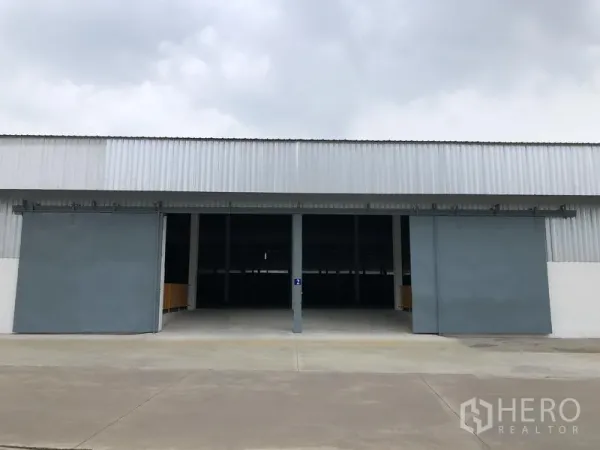 Warehouse for rent in Nonthaburi - Front view of a modern warehouse with two large sliding steel doors and a wide concrete driveway.