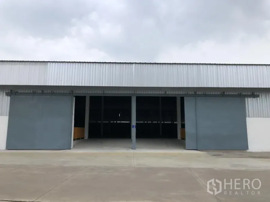 Warehouse for rent in Nonthaburi - Front view of a modern warehouse with two large sliding steel doors and a wide concrete driveway.