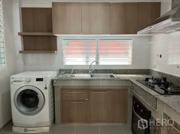Detached House for rent in Bang Kapi, Bangkok - Fitted kitchen with wood cabinets, granite countertops, gas hob, hood, oven, and a washing machine under the counter.