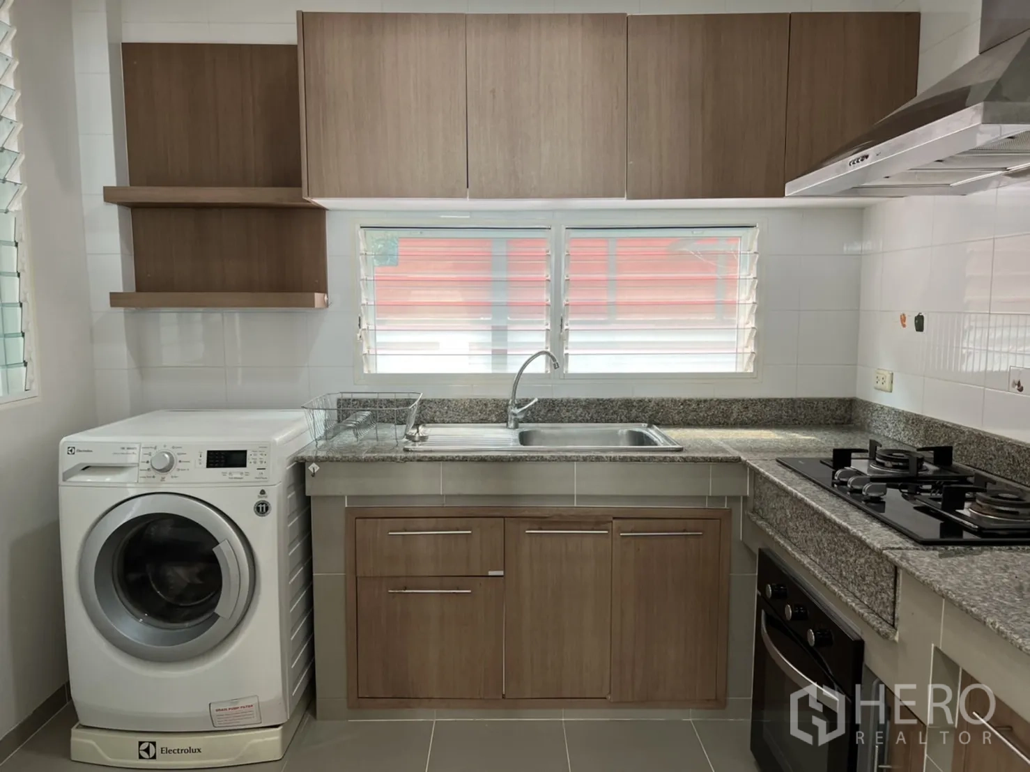Detached House for rent in Bang Kapi, Bangkok - Fitted kitchen with wood cabinets, granite countertops, gas hob, hood, oven, and a washing machine under the counter.