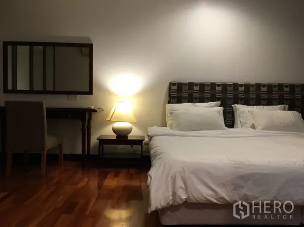 Condominium for rent in Watthana, Bangkok - Master bedroom with king bed, bedside lamp, dressing table, and warm wooden flooring.