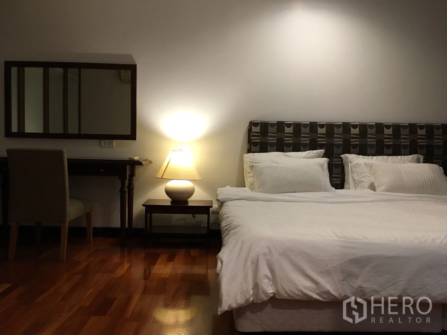 Condominium for rent in Watthana, Bangkok - Master bedroom with king bed, bedside lamp, dressing table, and warm wooden flooring.