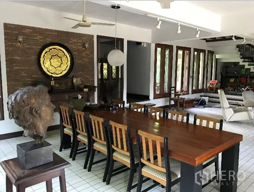Detached House for rent in Khlong Toei, Bangkok - Large dining room with a long wooden table, brick feature wall, and ceiling track lights.