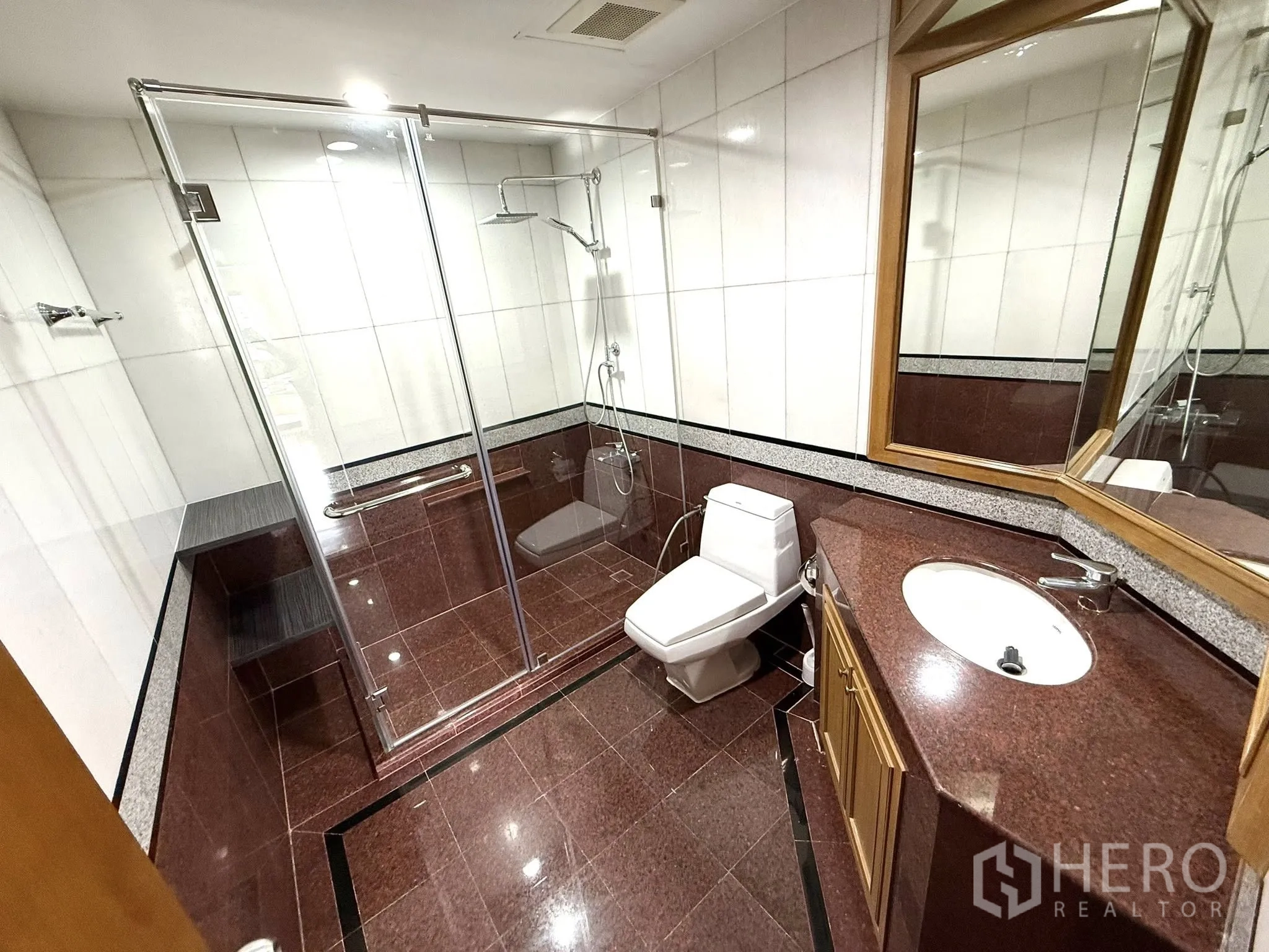 Condominium for rent in Sathon, Bangkok - Large bathroom with glass shower enclosure, vanity and stone tiles.