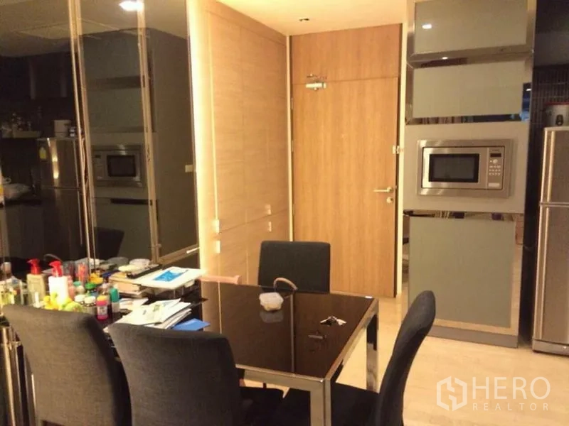 Condominium for rent in Watthana, Bangkok - Dining area with a glass-top table and four chairs next to a mirrored wall.