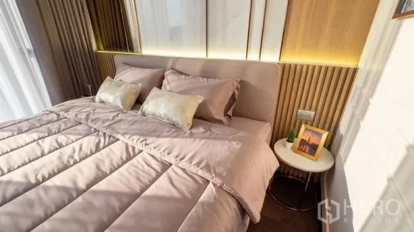 Condominium for rent in Watthana, Bangkok - Cozy bedroom with upholstered headboard, warm wood paneling, and bedside table.