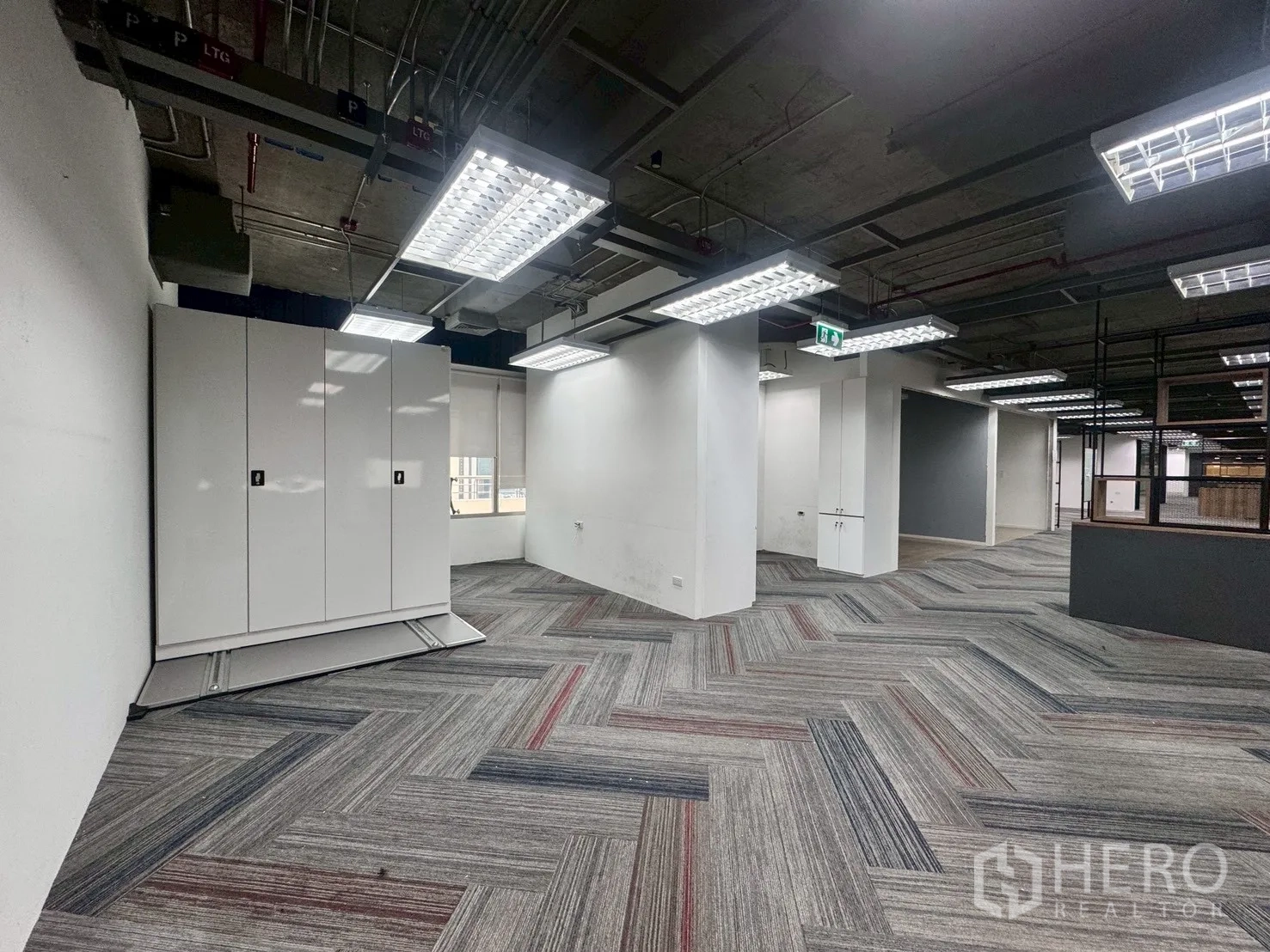 办公室 for rent in Watthana, Bangkok - 工作区铺人字纹地毯，裸露天花，靠窗设白色储物柜。